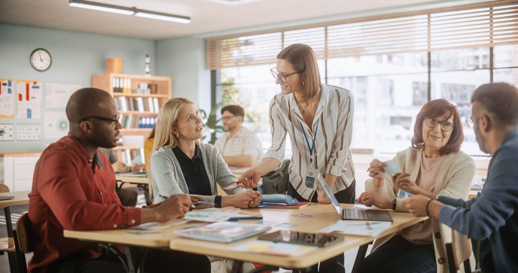 A group of school staff meet around a table while a colleague facilitates the discussion.