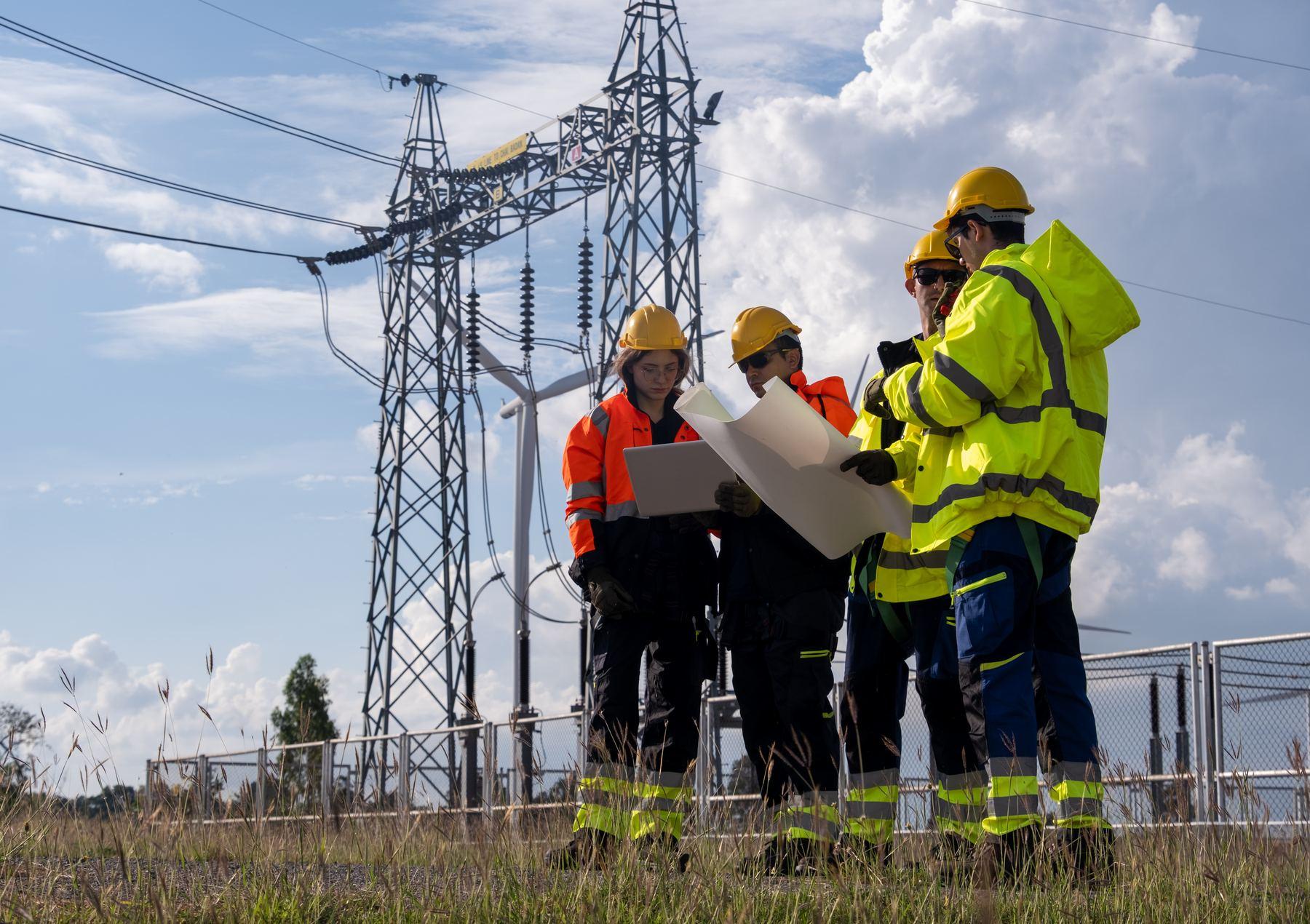 Four utility field workers in high-visibility gear review plans beside electrical infrastructure.